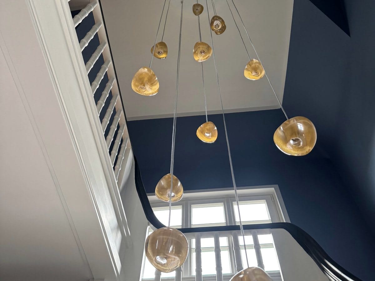 Saniertes Treppenhaus mit tiefblauer Wand, weißem Geländer und Glasleuchten